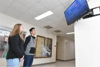 A male and female student viewing a digital display mounted on a wall